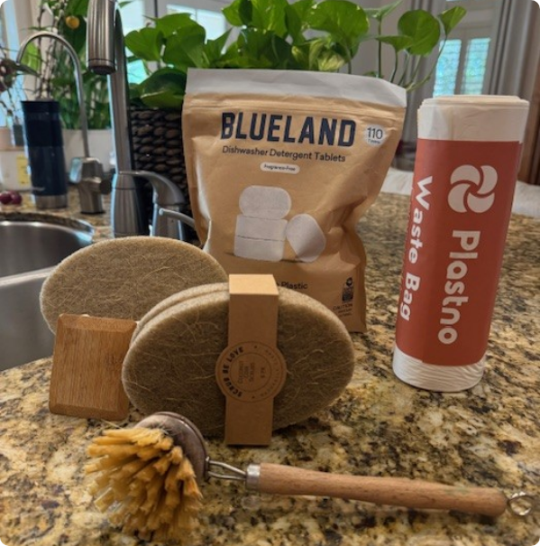 Plastic-free kitchen essentials including dishwasher tablets, compostable waste bags, and wooden dish brushes.